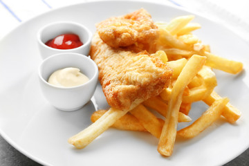 Plate with tasty fried fish, chips and sauces on table, closeup