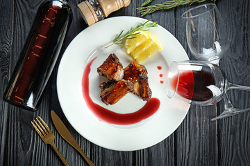 Plate with delicious ribs, bottle of wine and glasses on table