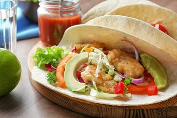 Wooden board with tasty fish tacos on table