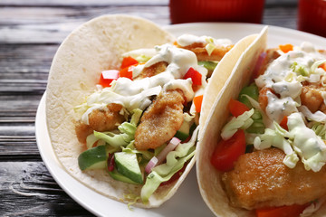 Plate with tasty fish tacos on wooden table