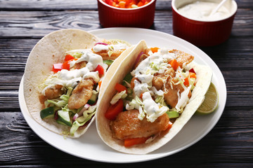 Plate with tasty fish tacos on wooden table