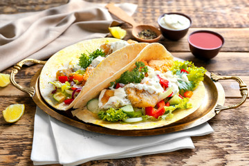Metal tray with tasty fish tacos and sauce on table