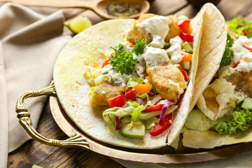 Metal tray with tasty fish tacos and sauce on table