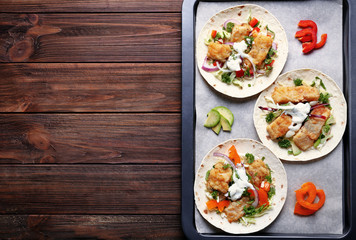 Baking tray with tasty fish tacos on wooden table