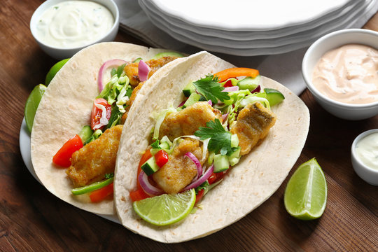 Plate with tasty fish tacos and sauces on wooden table