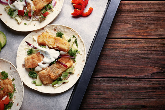 Baking tray with tasty fish tacos on wooden table