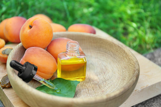 Bottle of essential oil and ripe apricots in wooden bowl outdoors