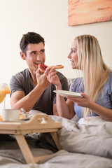 Happy young couple eating bread and strawberry jam while having breakfast in bed