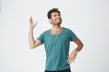Fototapeta premium Expressive smiling handsome young spanish man in blue t-shirt, listening his favourite song with headphones and dancing happily. People and lifestyle concept