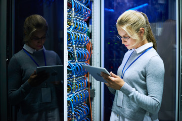 Portrait of young smiling woman checking data on digital tablet while working with supercomputer in...