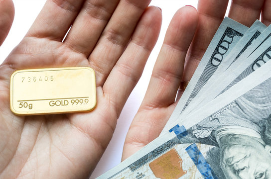 Gold bullion and hundred-dollar bills in the hands of a man.