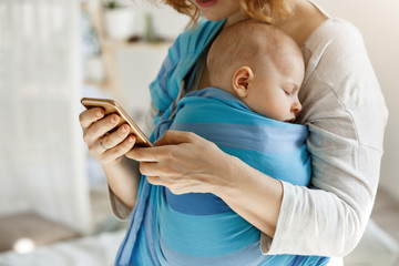 Cute tiny kid napping peacefully while mother hugging him and texting husband by phone asking buy...