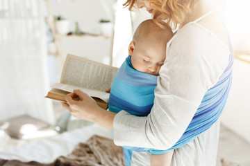 Close up of young mom reading fairy tales for her newborn little son in comfortable light bedroom....