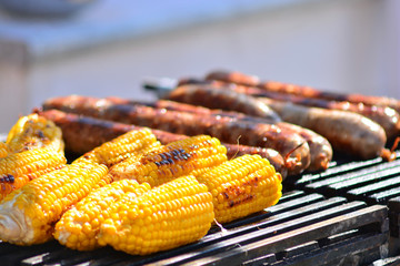Street food restaurant. The cook prepares on the grill delicious corn and sausages. 