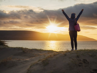 Sunset over Atlantic ocean, West coast of Ireland, a woman with her hands high, showing excitement.