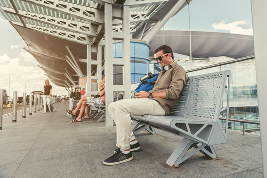 Cheerful stylish man is resting on seats and using mobile