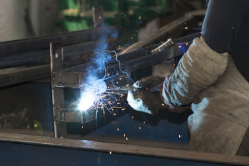 Metalworking shop workers work behind machines and apparatuses to create steel structures.