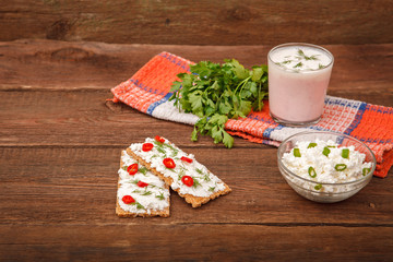 Bread with cream cheese and a bowl of cottage cheese with herbs, with a glass of kefir, yogurt and chili peppers on a wooden background. Proper nutrition. Breakfast.