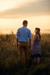 Holding hands loving couple stands in the middle of the wheat field at sunrise or sunset