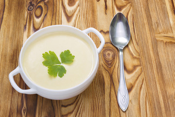 Tasty potato soup with a leaf of parsley, rustic wooden table. Potato and onion vegan, vegetarian healthy cream soup in white ceramic bowl and a spoon. Traditional lunch or dinner.