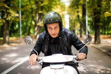 Handsome man riding a scooter on city streets on summer day. Closeup portrait of happy smiling young male on vintage scooter