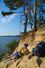 Boy sitting on sand cliff looking to sea. Travel and tourism concept