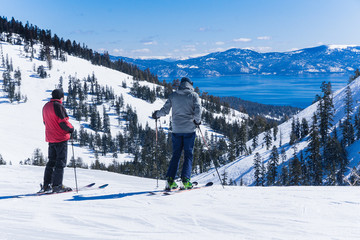 Two middle aged men on skis look out over the lake tahoe mountains - obrazy, fototapety, plakaty