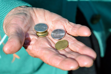 The coins are in the hands of the old lady. An elderly woman with money in her hands. Poverty alms