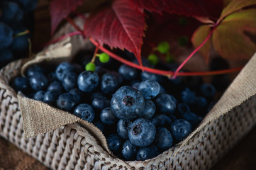 Blue berries blueberries in wicker white basket with autumn leaves in a rustic style. Close-up.