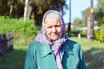 An old woman in a scarf. Portrait of a lonely old woman standing in a village