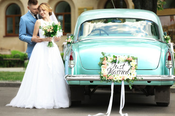 Happy wedding couple near decorated car, outdoors