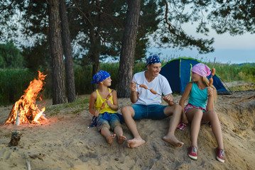 happy family roasting sausages over campfire. camping and tourism concept