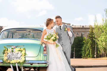 Happy wedding couple near decorated car outdoors