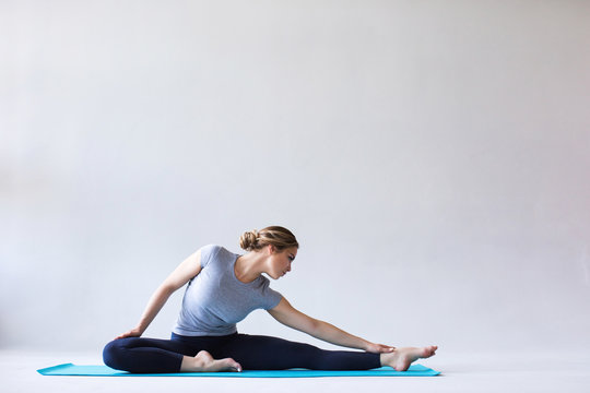 Young beautiful woman in sportswear doing stretching while sitting on the floor on yoga mat.