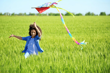 Happy little Afro American girl with kite in green field