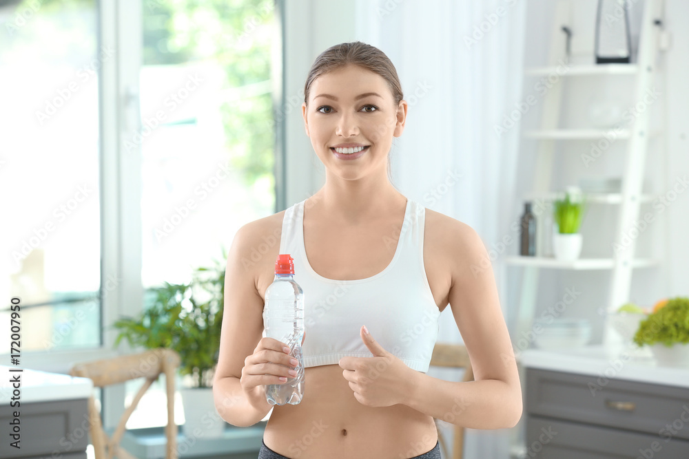 Wall mural Beautiful young woman with bottle of water at home. Diet concept