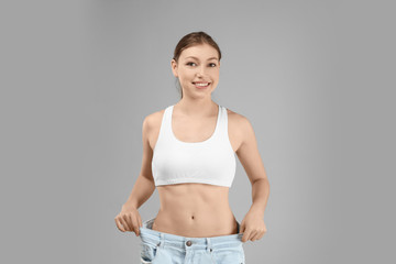 Beautiful young woman in oversized jeans on gray background. Diet concept