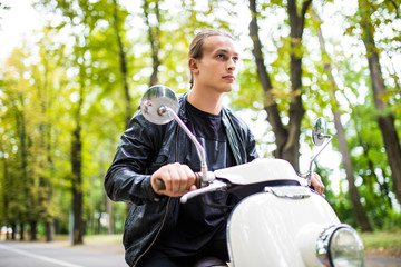 fashionable young man riding a vintage scooter in the street