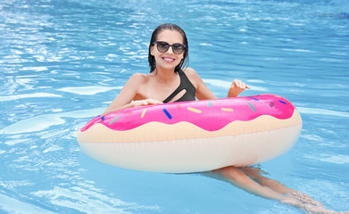 Beautiful young woman with inflatable donut in swimming pool
