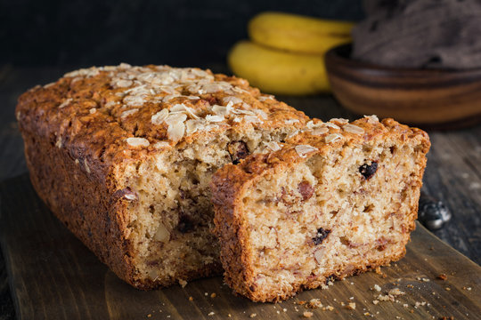 Sliced banana bread loaf with walnuts and oats on wooden cutting board. Closeup view, horizontal