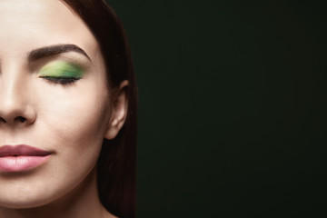 Fototapeta premium Young beautiful woman with fancy green makeup on dark background