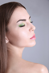 Naklejka premium Young beautiful woman with fancy green makeup on grey background