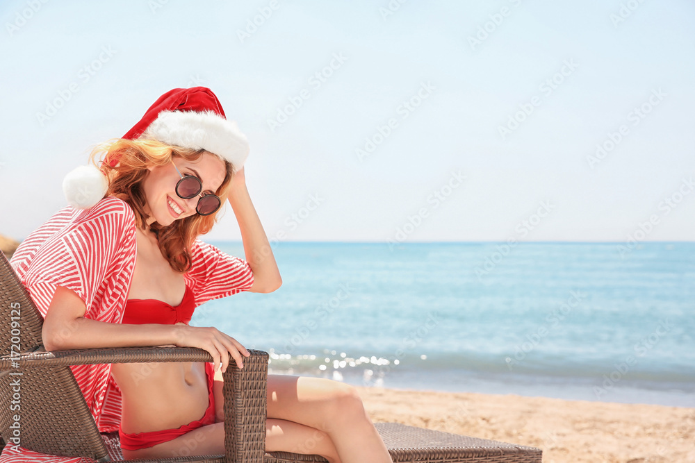 Wall mural young woman in santa hat on beach. christmas holidays concept