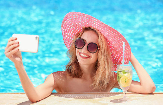 Beautiful young woman taking selfie in swimming pool