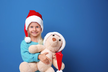 Cute girl in Santa hat with toy on color background