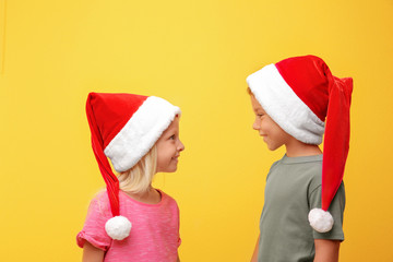 Cute children in Santa hats on color background