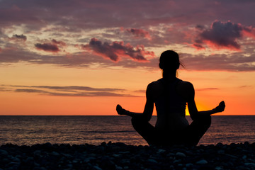 Woman meditating on the beach in lotus position. Silhouette, sunset