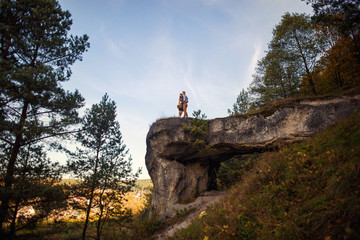 Sensual lovely couple in warm hugs on casual clothes staying on the top of the rock at sunrise or sunset. Love story concept