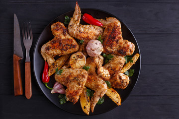 Grilled chicken wings on black plate decorated with garlic and spices, free space for advertisement or text. Cooking concept, meat dishes, homemade food