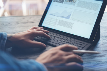 View of male hands typing on electronic tablet keyboard-dock station. Business information on device screen. Man working at office.Horizontal.